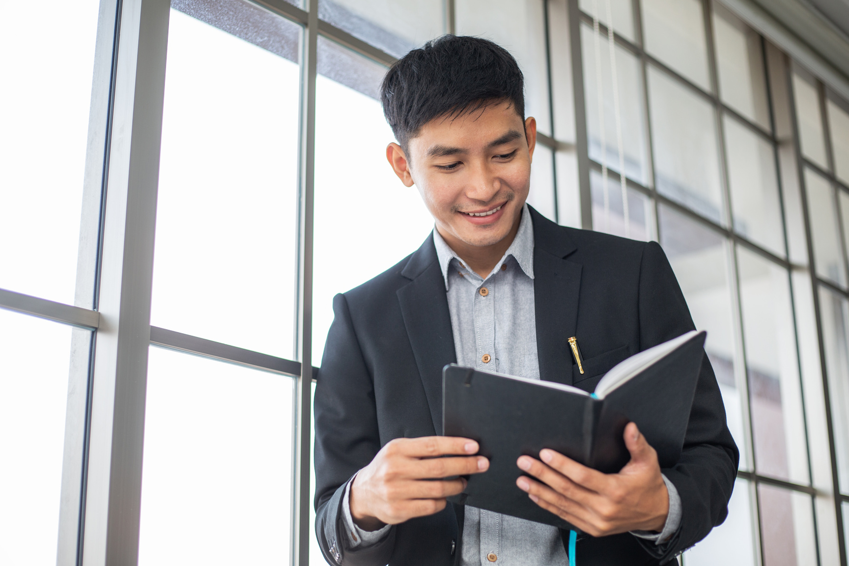 Asian Male Employee Reading Book in Corporate Office.
